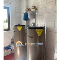 Słoneczny Doradca PL Sp. z o.o. - Dwa zbiorniki buforowe Technix w kotłowni z białymi płytkami, wyposażone w niebieski i szary zbiornik wyrównawczy ciśnienia, widoczne rury i manometry.