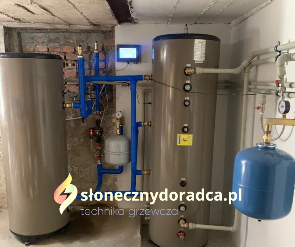 Dwa zbiorniki akumulacyjne ciepła z niebieską instalacją hydrauliczną i panelem sterowania w kotłowni w Ostrowie Wielkopolskim.