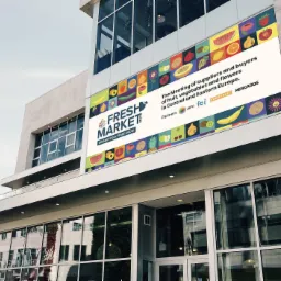 Budynek z zamontowanym banerem reklamowym Fresh Market 2022 z motywami owoców i warzyw, informujący o spotkaniu dostawców i kupców w Europie Środkowej i Wschodniej.