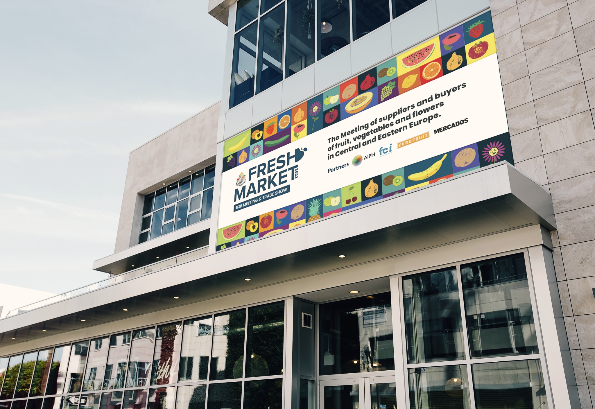 Budynek z zamontowanym banerem reklamowym Fresh Market 2022 z motywami owoców i warzyw, informujący o spotkaniu dostawców i kupców w Europie Środkowej i Wschodniej.