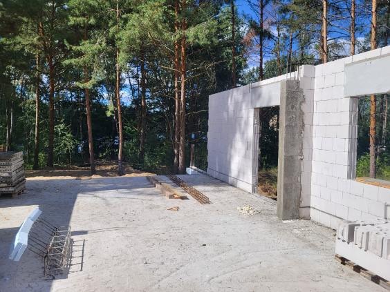 Budowa domu murowanego w lesie: ściany z białych bloczków, widoczne zbrojenia i materiały budowlane na placu budowy.