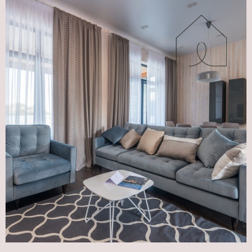 Salon w odcieniach szarości z wzorzystym dywanem, zasłonami w geometryczny wzór i szarą sofą z poduszkami, oświetlony naturalnym światłem.