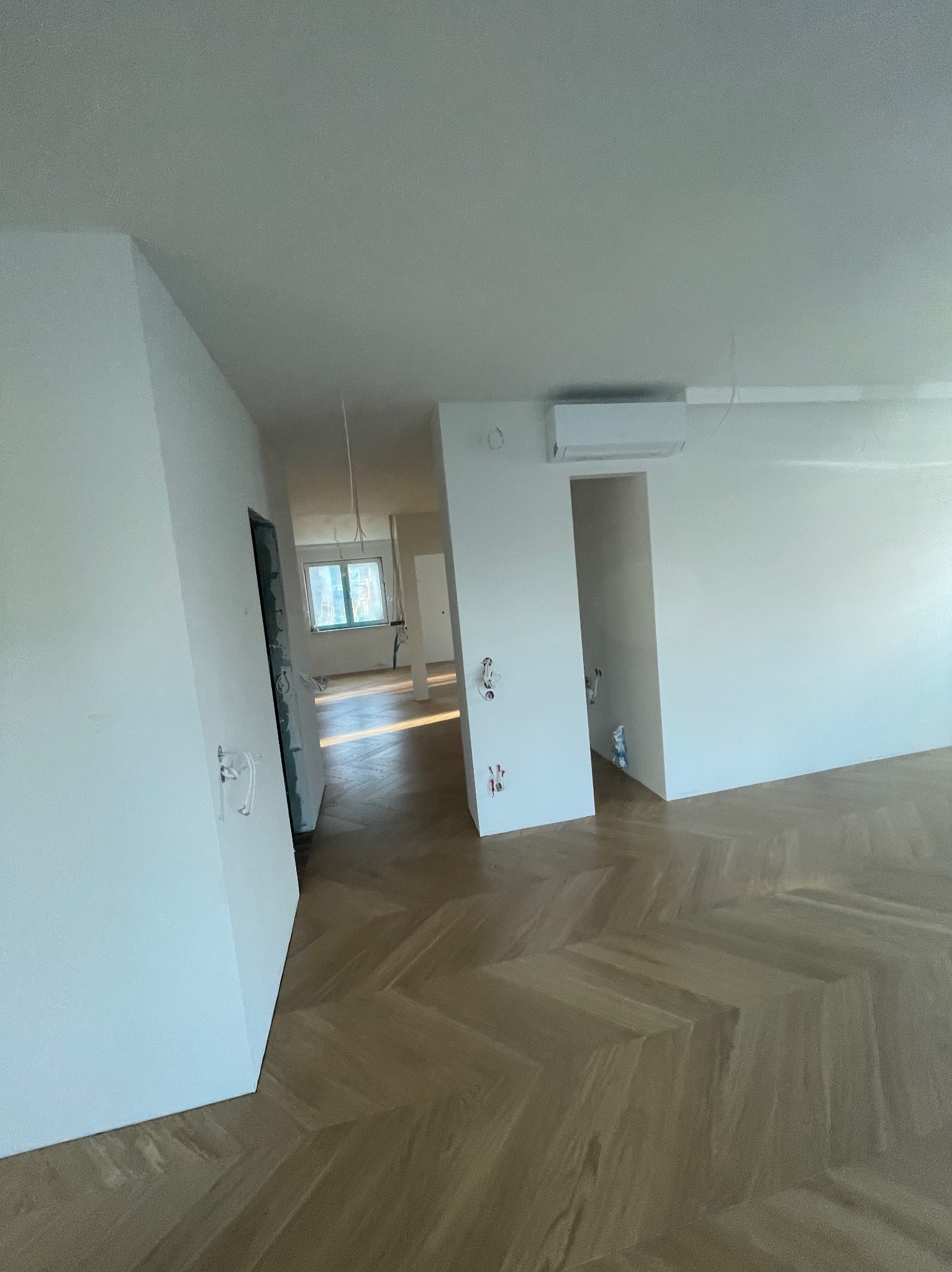 Wnętrze mieszkania po remoncie: gładkie, białe ściany, parkiet ułożony we wzór jodełki, widoczne instalacje elektryczne przed montażem osprzętu, klimatyzator na ścianie.