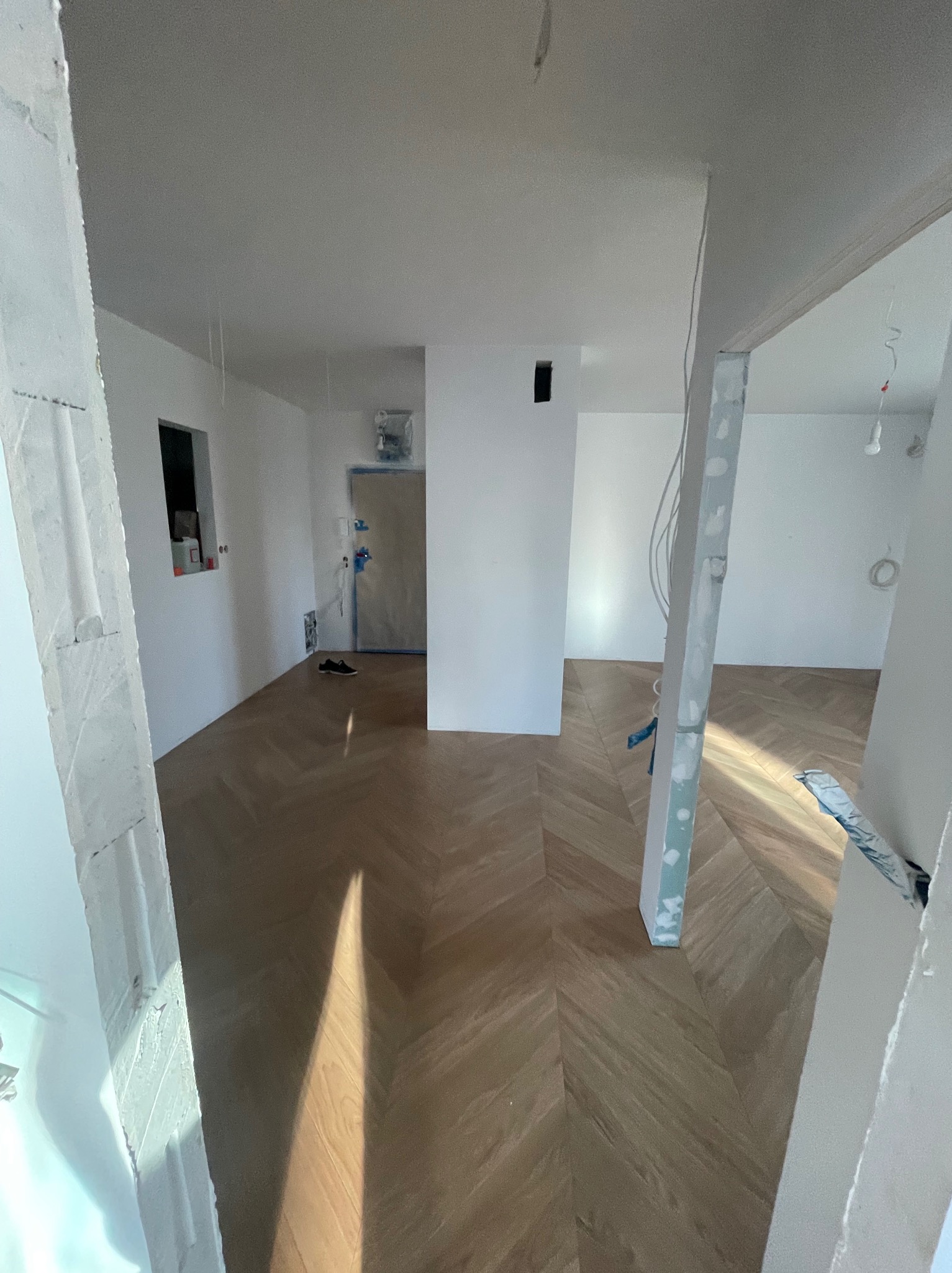 Wnętrze w trakcie remontu: parkiet ułożony w jodełkę, ściany przygotowane do dalszych prac wykończeniowych, widoczne ślady po szpachlowaniu na framudze drzwi.