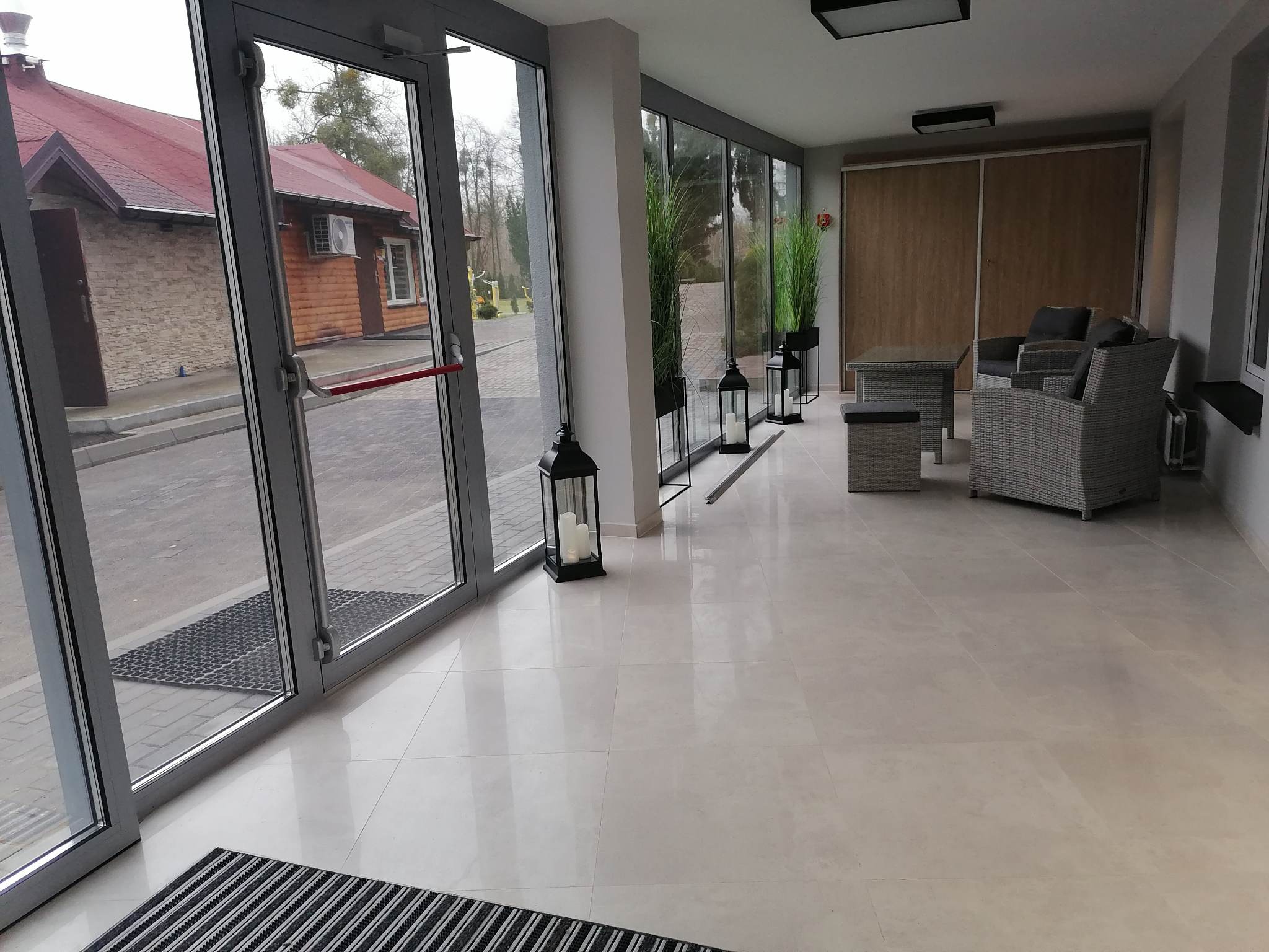 Jasna, błyszcząca podłoga z płytek w przeszklonym pomieszczeniu z wiklinowymi meblami i dekoracyjnymi lampionami.