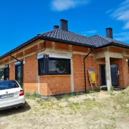 Dom w trakcie budowy z zamontowanymi roletami zewnętrznymi w kolorze czarnym, widoczny samochód Skoda Rapid na podjeździe.