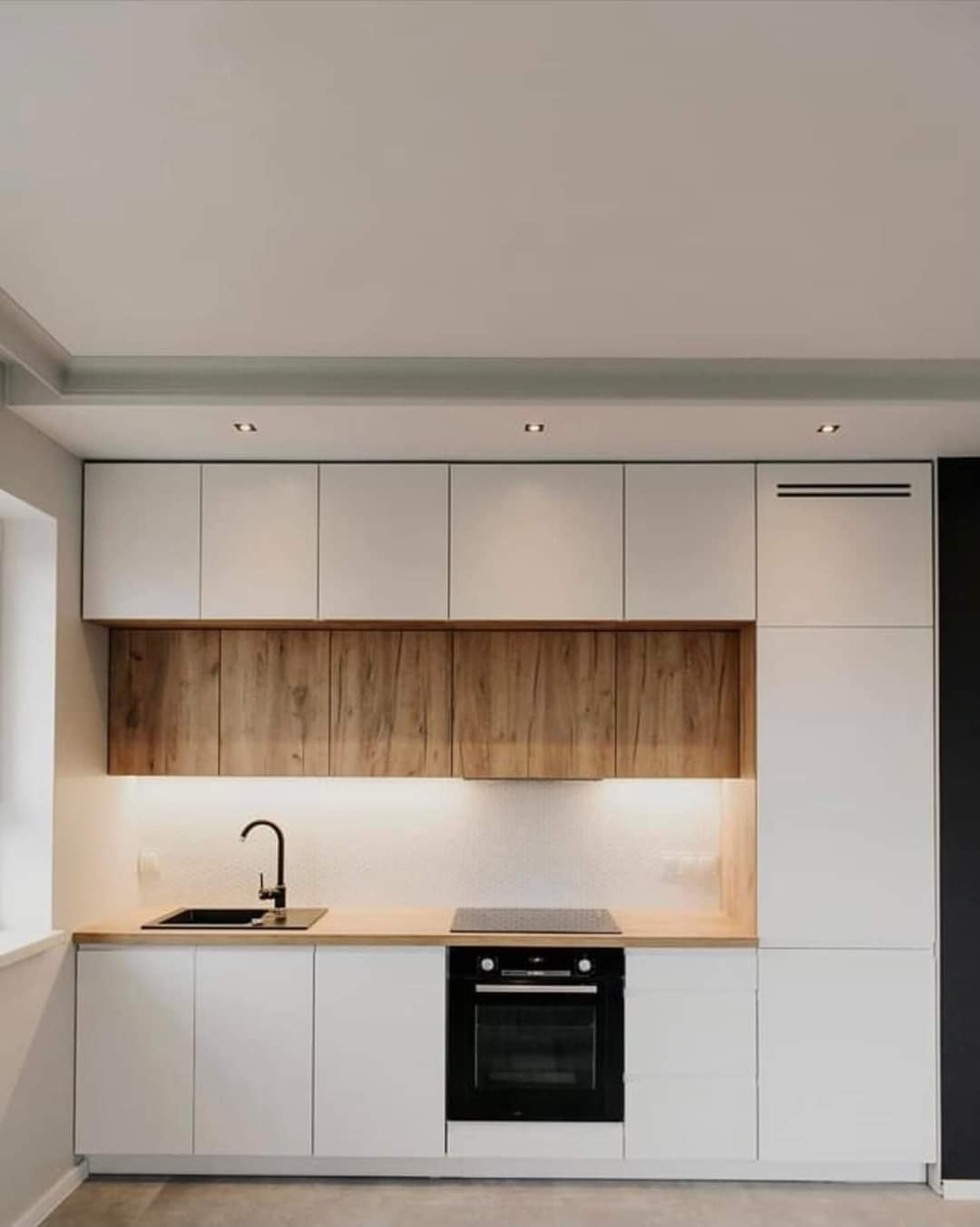 Nowoczesna kuchnia z białymi szafkami, drewnianymi frontami górnych szafek i drewnianym blatem, oświetleniem LED pod szafkami i czarnym zlewem.