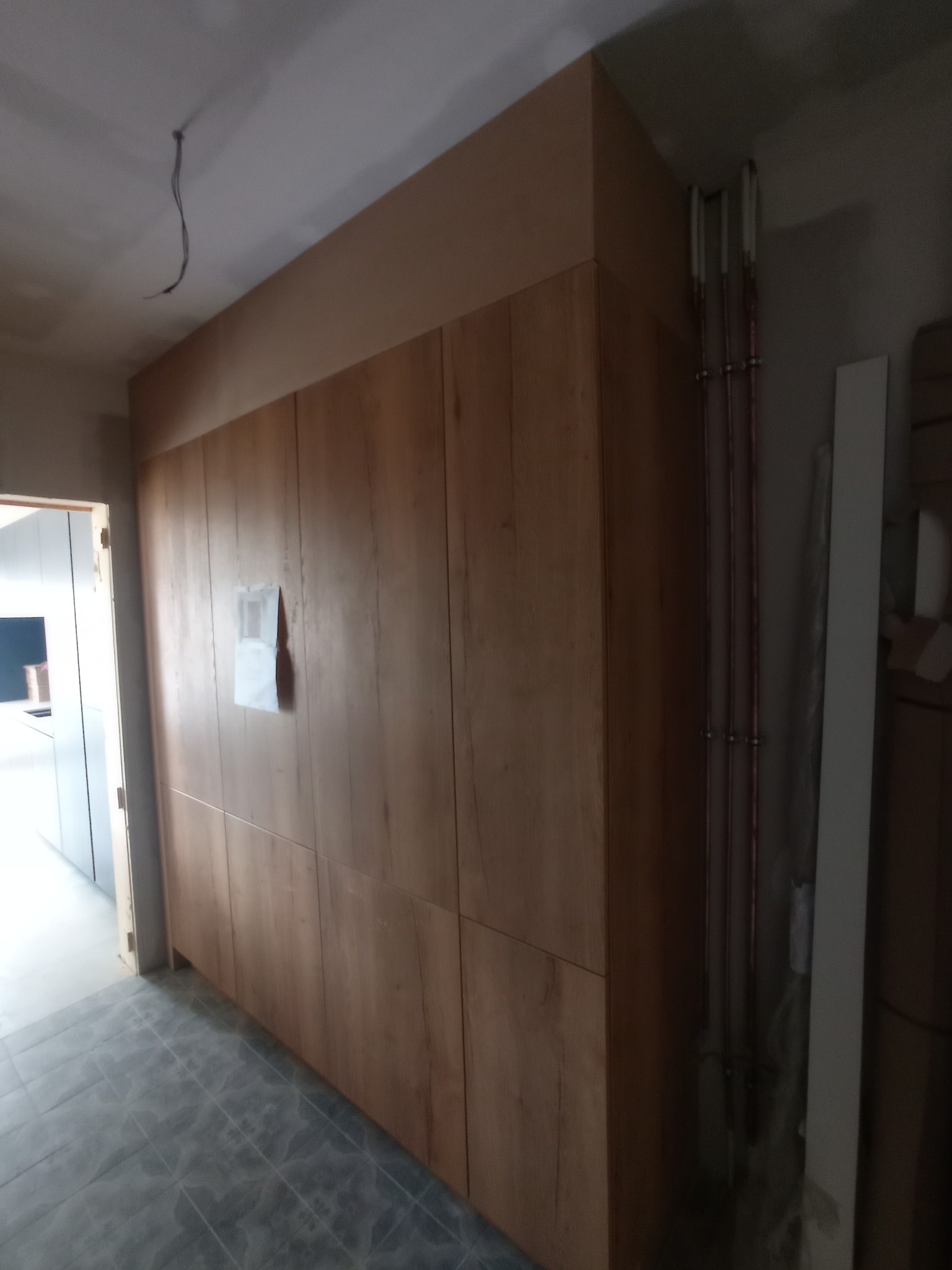 Drewniana zabudowa ściany z widocznymi pionowymi rurami instalacyjnymi w surowym wnętrzu, z niedokończonym wykończeniem sufitu.