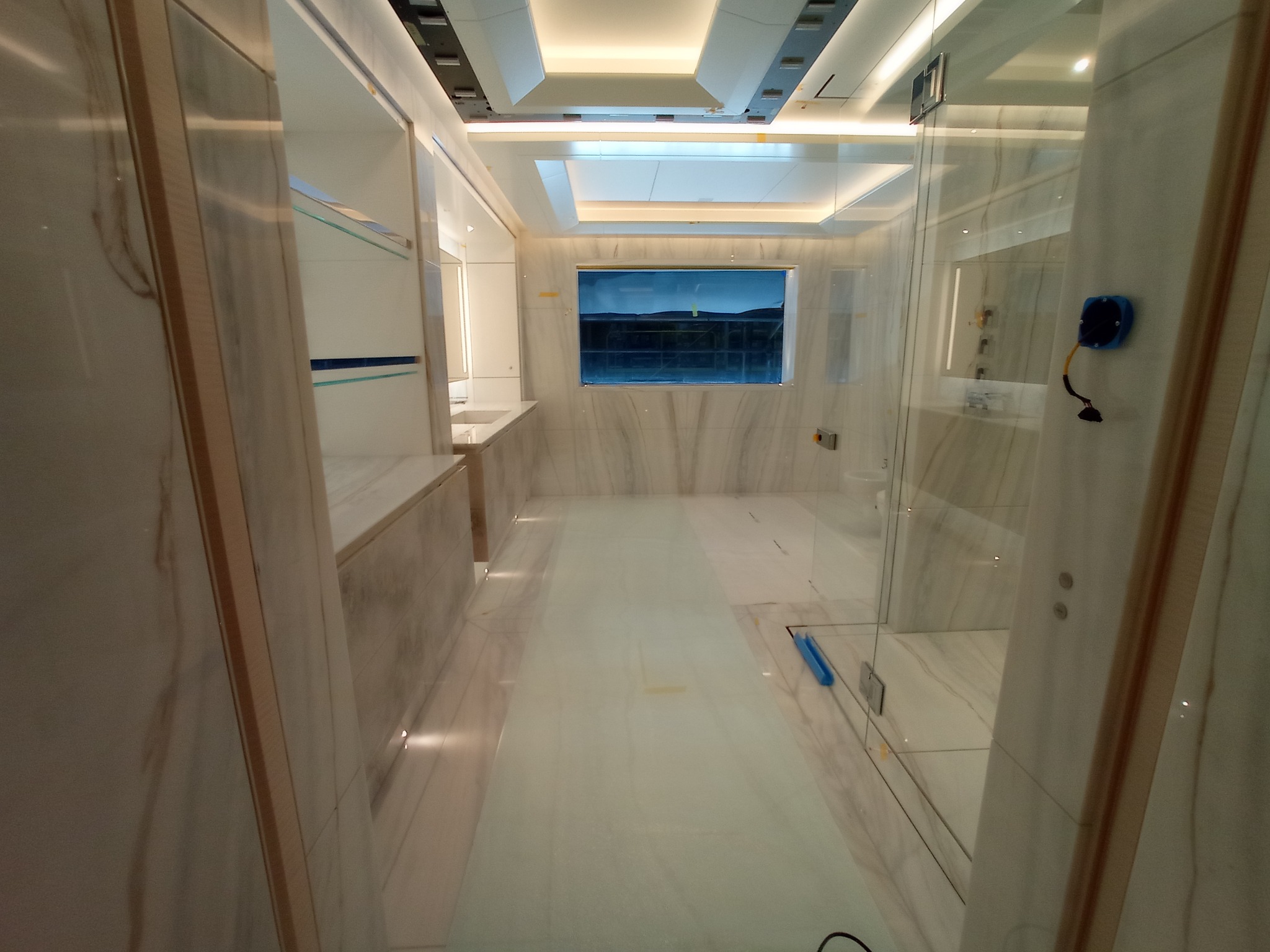 Nowoczesna łazienka w trakcie wykańczania w Łopusznie, widoczne marmurowe ściany i podłoga, szklana kabina prysznicowa oraz częściowo zamontowane szafki z drewnianymi elementami.