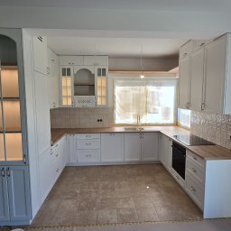 Woodii Damian Mrzygłód - Jasna kuchnia w stylu klasycznym z drewnianymi blatami i przeszklonymi szafkami, oświetlona od wewnątrz, z widocznymi elementami wykończeniowymi.