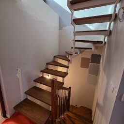 Woodii Damian Mrzygłód - Nowoczesne schody drewniane z białymi elementami konstrukcyjnymi, oświetleniem punktowym na ścianie i próbkami kolorów farb na ścianie, widziane z dołu.