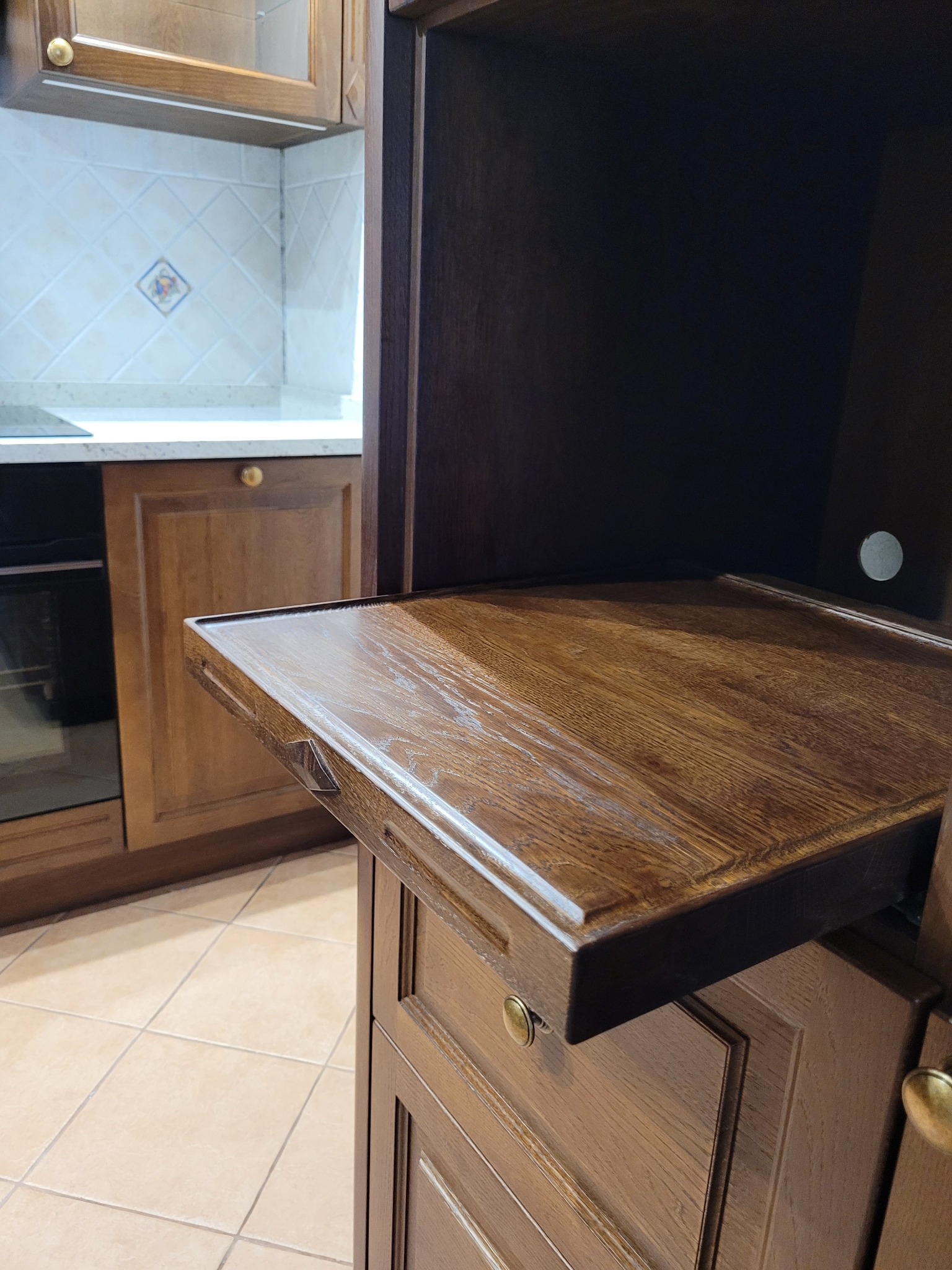 Wysuwany, lakierowany blat z ciemnego drewna w zabudowie kuchennej, widoczny fragment frontu szafki z ozdobnym frezem i okrągłym uchwytem.