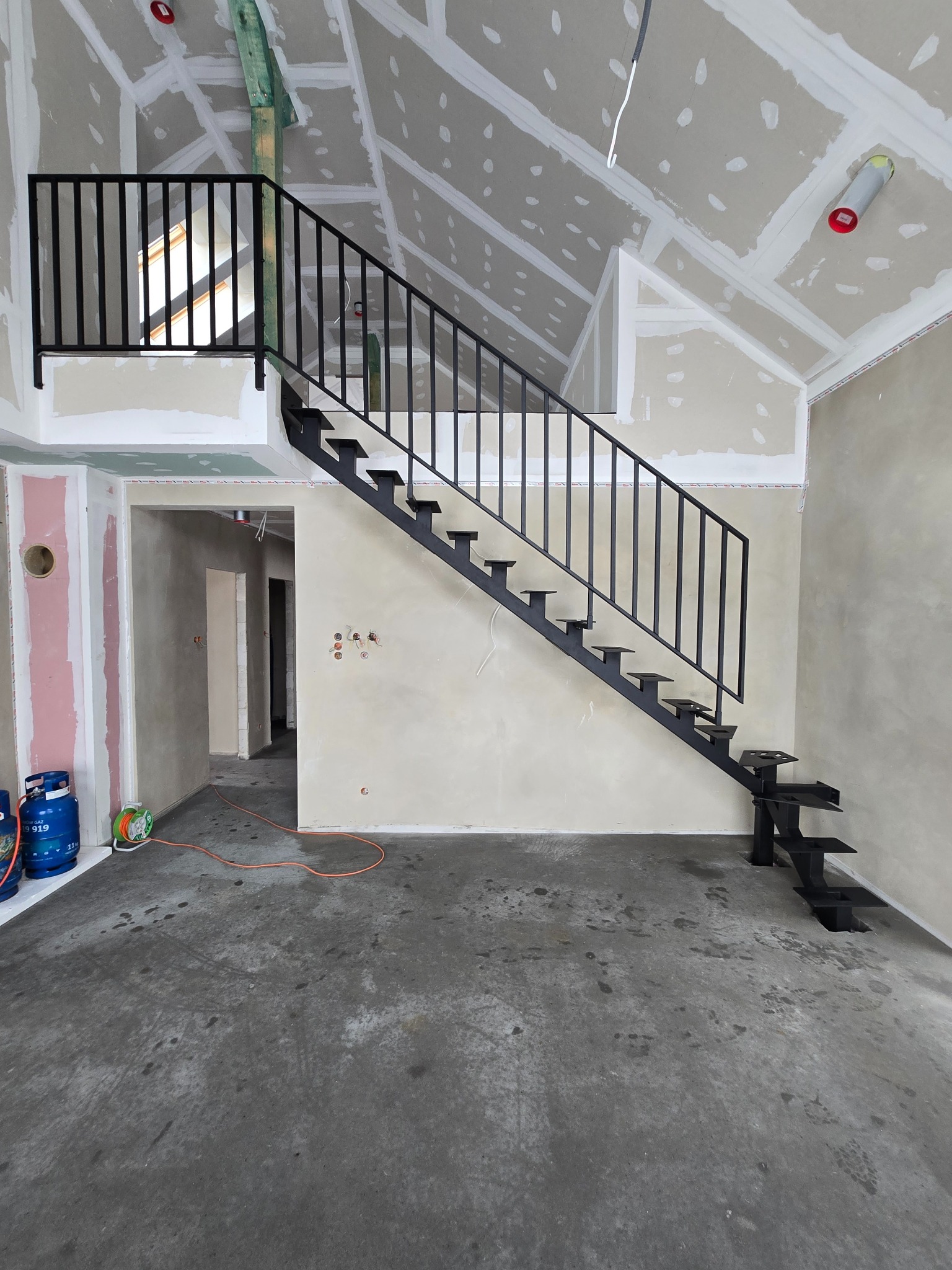 Montaż schodów metalowych w surowym wnętrzu z płytami gipsowymi i widoczną instalacją elektryczną. Minimalistyczny design schodów.