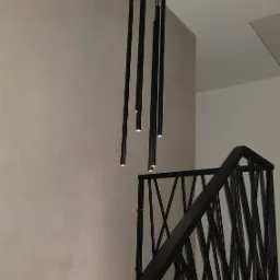 Nowoczesna lampa wisząca z czarnymi, cylindrycznymi kloszami nad czarną balustradą schodów w jasnym wnętrzu.