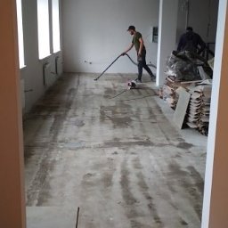 Firma remontowo-wykończeniowa AIRUS sp. z o.o. - Przygotowanie podłoża pod posadzkę w Warszawie: pracownik odkurza wylewkę samopoziomującą przed dalszymi pracami wykończeniowymi, widoczne płyty i narzędzia.