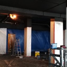 Firma remontowo-wykończeniowa AIRUS sp. z o.o. - Przygotowanie do malowania wnętrza: kolumny zabezpieczone folią, ściany osłonięte niebieską plandeką, drabina, puszki z farbą i akcesoria malarskie w słabo oświetlonym pomieszczeniu.