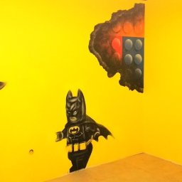 Firma remontowo-wykończeniowa AIRUS sp. z o.o. - Żółta ściana z malunkiem Batmana z klocków Lego, obok imitacja dziur w ścianie z widocznymi klockami.