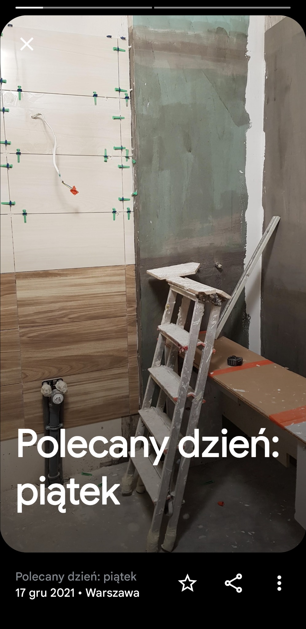 Ściana łazienki w trakcie układania płytek imitujących drewno, z widocznymi krzyżykami dystansowymi, obok ściana przygotowana pod tynk, drabina malarska, rury instalacji wodnej.