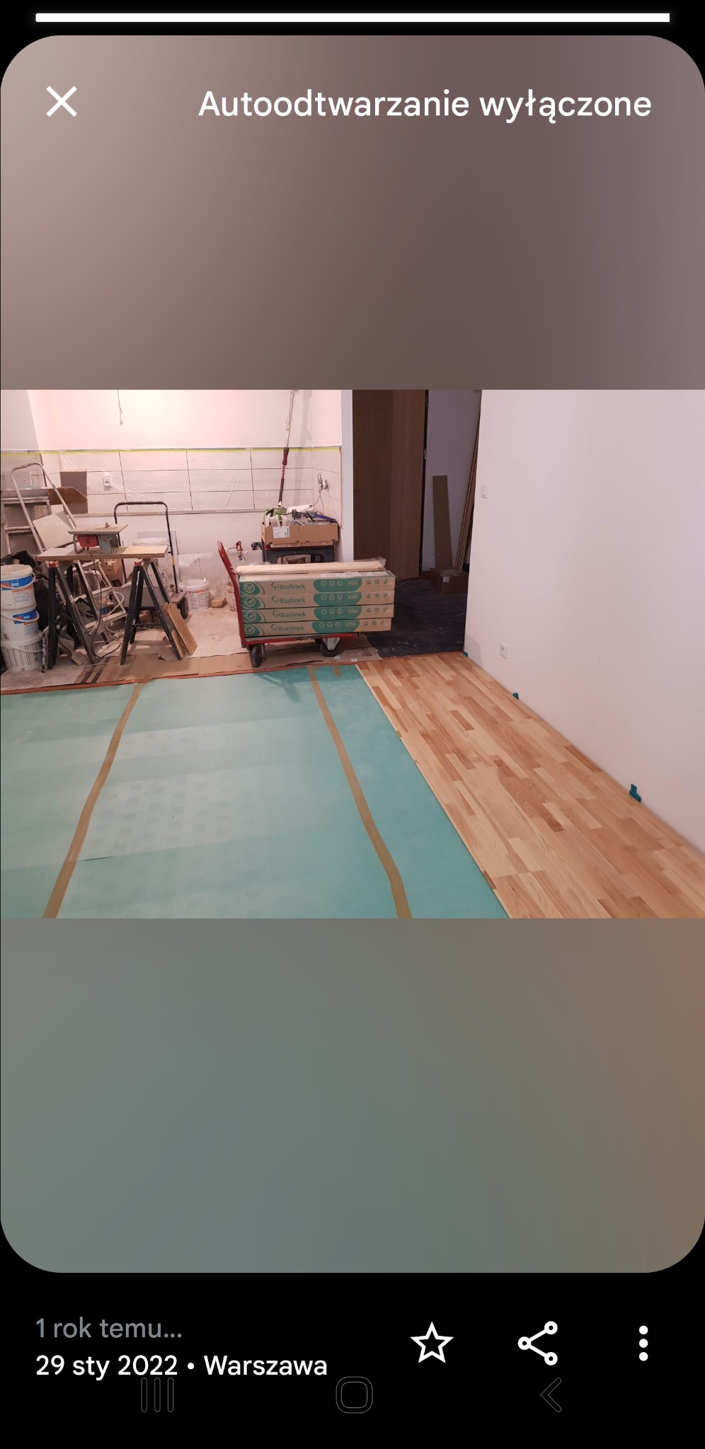 Układanie drewnianej podłogi w Piasecznie: widoczny fragment ułożonej podłogi, podkład zabezpieczony taśmą, wózek z paczkami paneli Barlinek oraz drabina i narzędzia w tle.