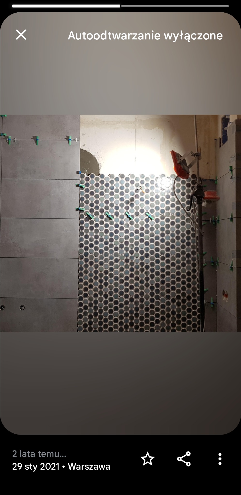 Układanie mozaiki z okrągłych płytek w łazience, widoczne poziome płytki w odcieniach szarości po lewej stronie i zielone kliny dystansowe.