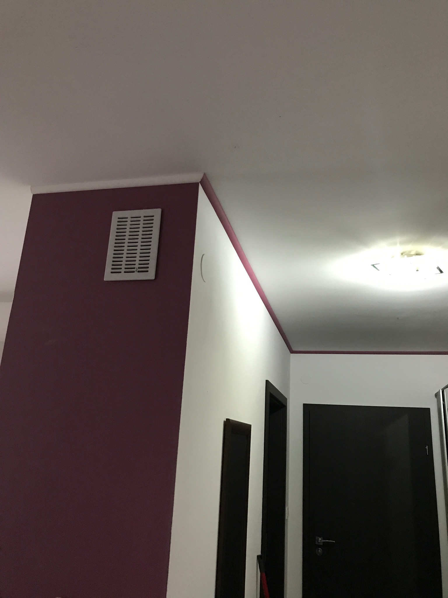 Pomieszczenie po odświeżeniu: ściana w kolorze burgundowym kontrastuje z bielą, widoczny fragment sufitu i drzwi.
