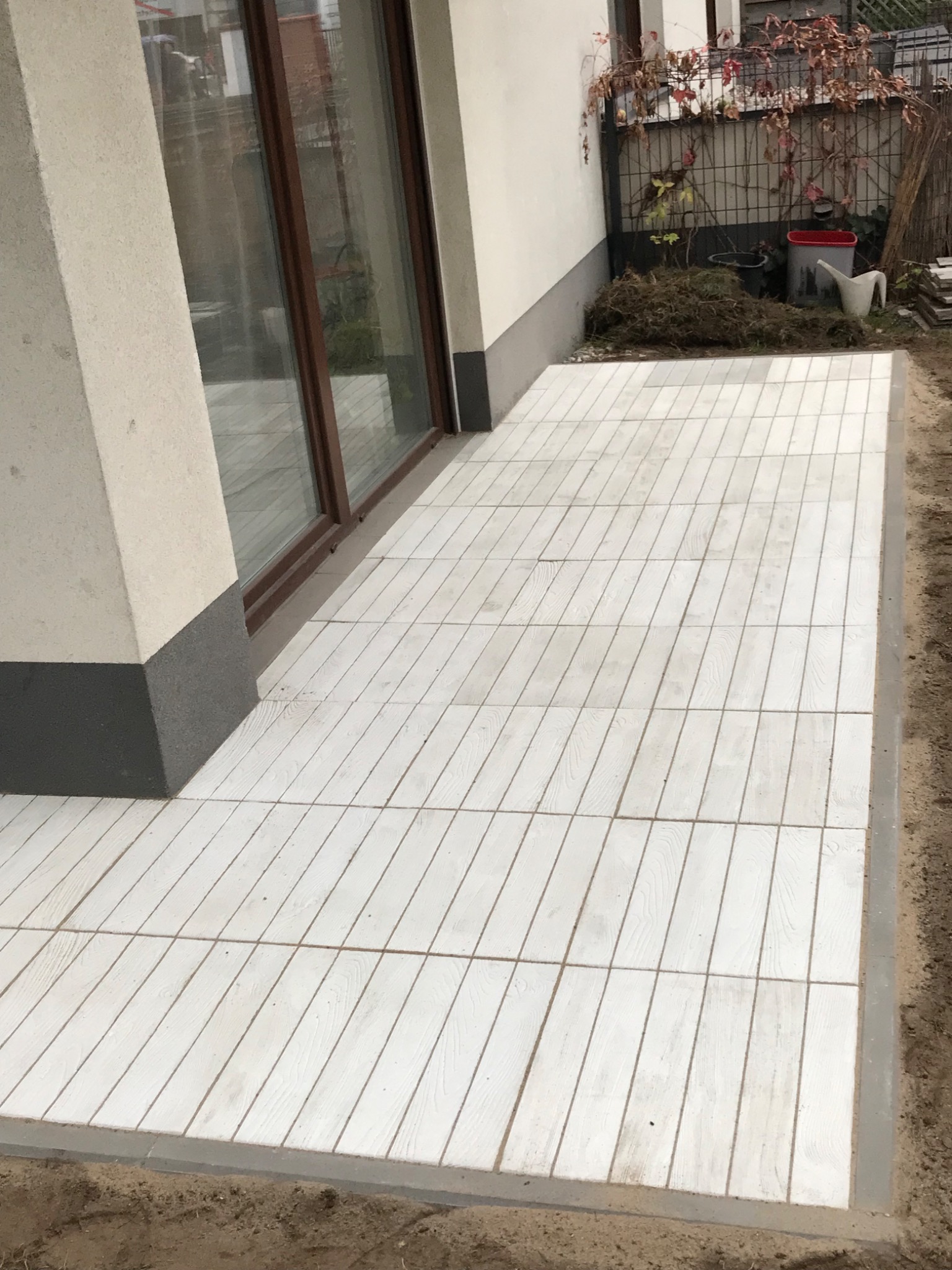 Biała kostka brukowa imitująca drewno ułożona na tarasie przy budynku, widoczne detale faktury i krawędzie.