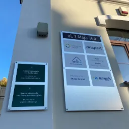 Tablica informacyjna na elewacji budynku z nazwami firm, w tym dwie kancelarie adwokackie: Adwokat Sandra Rabae i Adwokat Żaneta Helena Leszczyńska, z numerami telefonów i adresami stron...