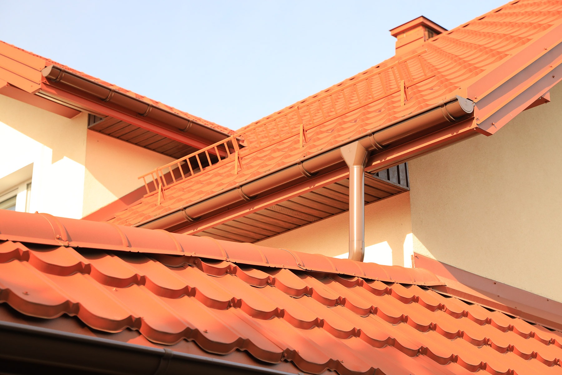 Blachodachówka Armano w odcieniach terakoty na dachu domu jednorodzinnego, z widocznym systemem rynnowym w kolorze brązowym i fragmentem elewacji.