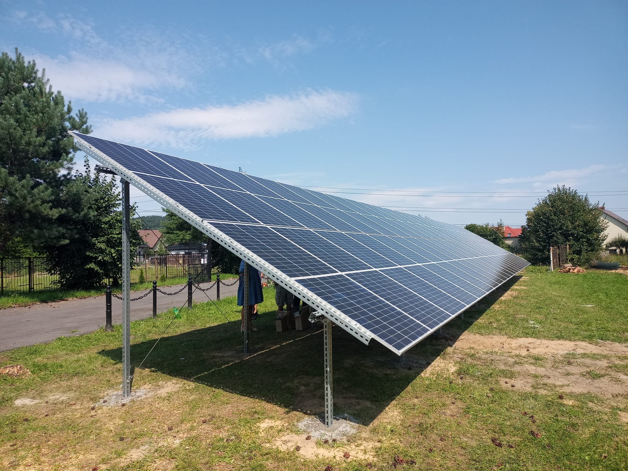 Instalacja paneli słonecznych w Krakowie na metalowej konstrukcji, widoczne częściowo osoby montujące, błękitne niebo w tle.
