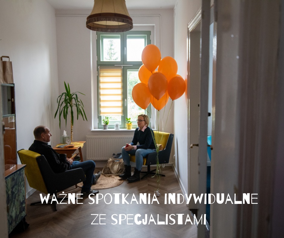 Gabinet z pacjentem i terapeutą podczas sesji, dekorowany pomarańczowymi balonami, widok z korytarza.