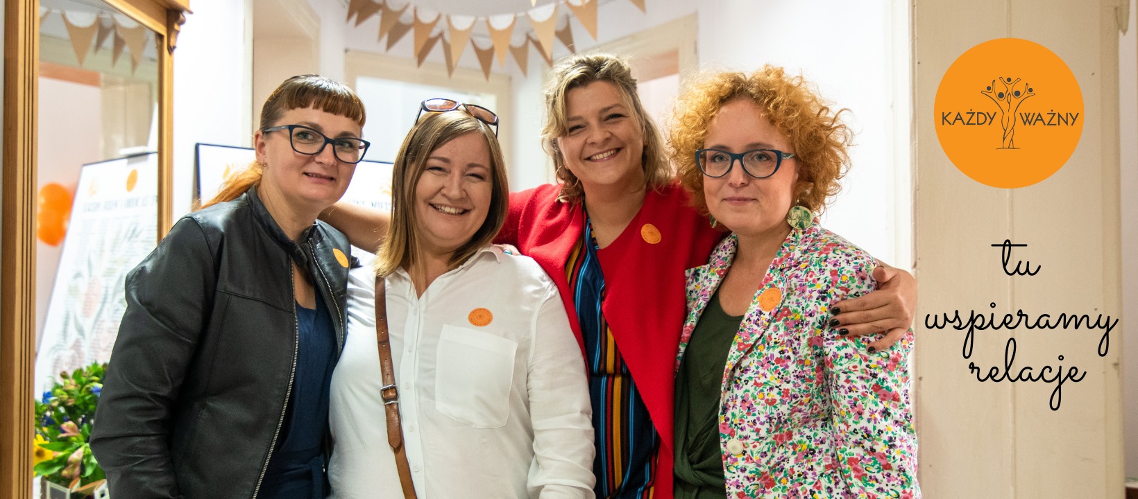 Cztery uśmiechnięte kobiety w różnym wieku, ubrane w kolorowe stroje, pozują razem w jasnym wnętrzu z dekoracjami i logo 'Każdy Ważny - tu wspieramy relacje'.