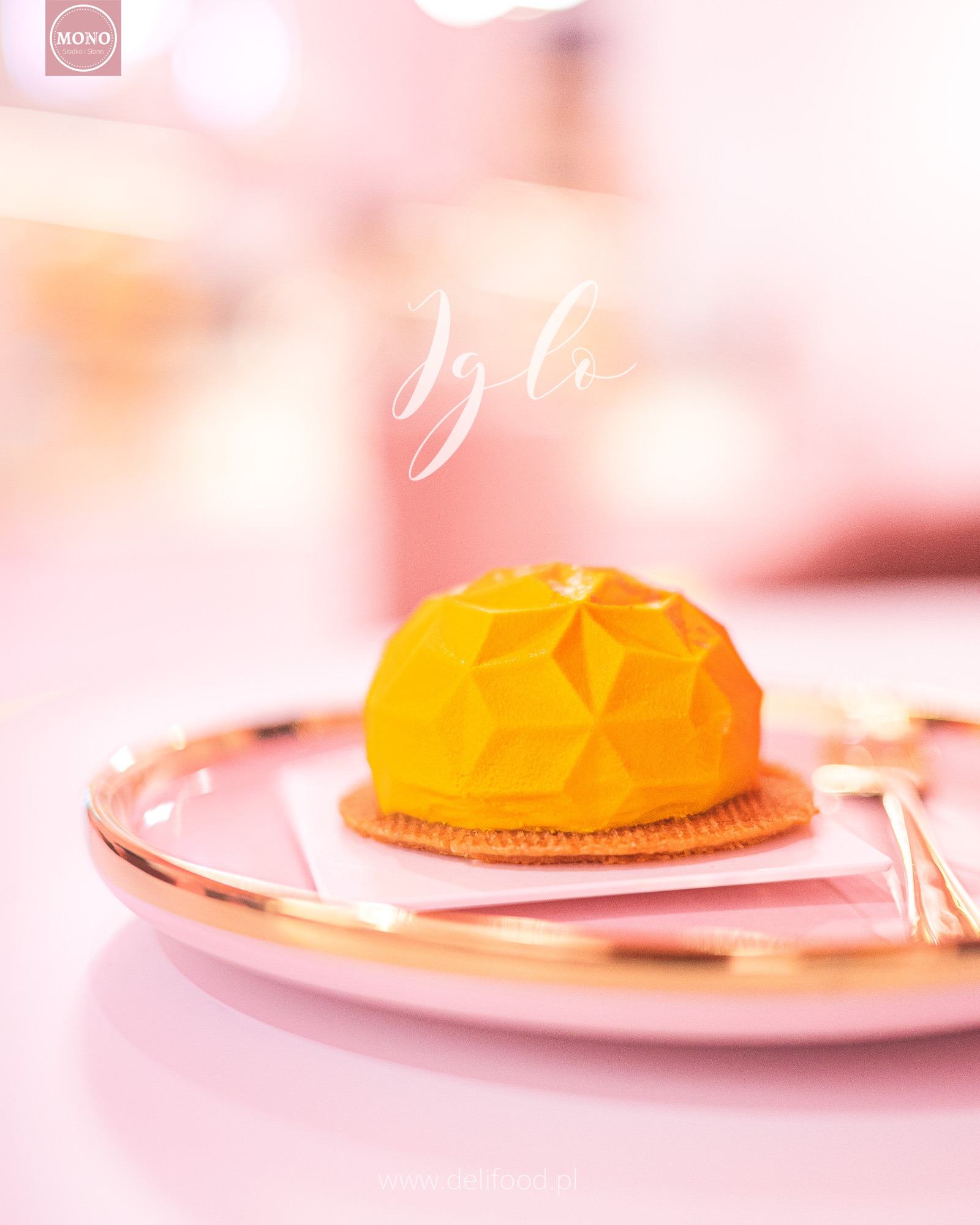 Żółty deser w kształcie kopuły z geometrycznymi podziałami, umieszczony na różowym talerzu ze złotym obramowaniem, na jasnoróżowym tle.