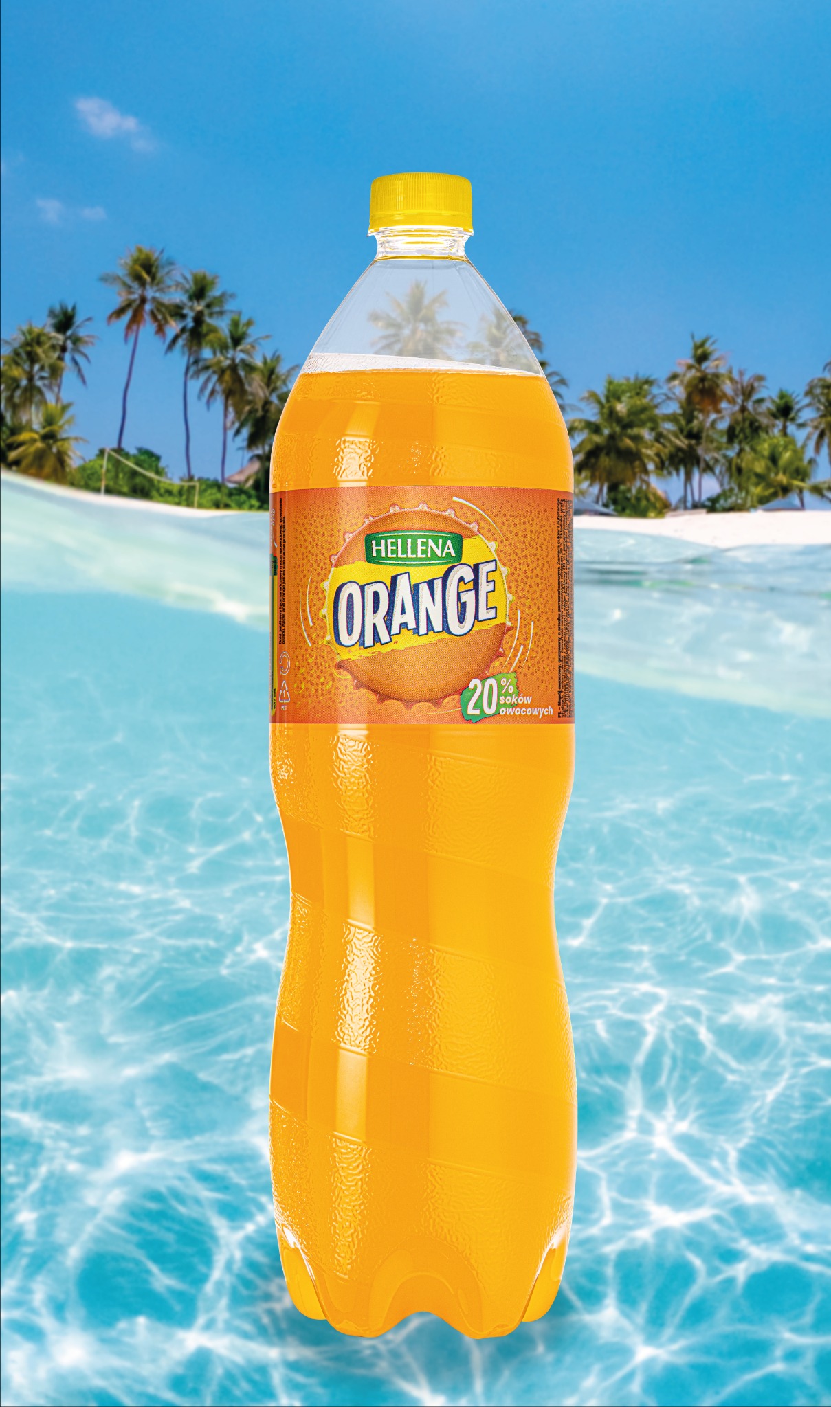 Butelka napoju pomarańczowego Helleny na tle tropikalnej plaży z palmami i błękitną wodą.