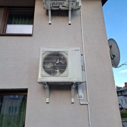 InstalTech Paweł Grochowski - Dwie jednostki zewnętrzne klimatyzacji Mitsubishi Electric zamontowane na beżowej elewacji budynku, z widocznymi oknami i białymi rurami instalacyjnymi.