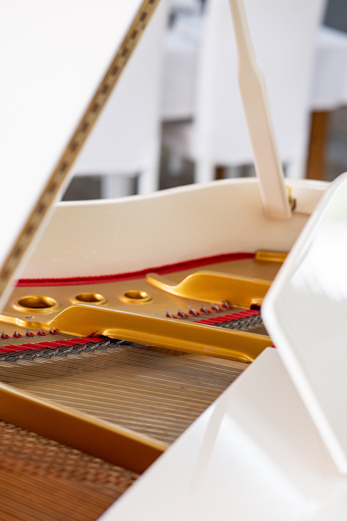 Wnętrze białego fortepianu z widocznymi złotymi elementami, czerwonym filcem i strunami, z perspektywy z bliska.
