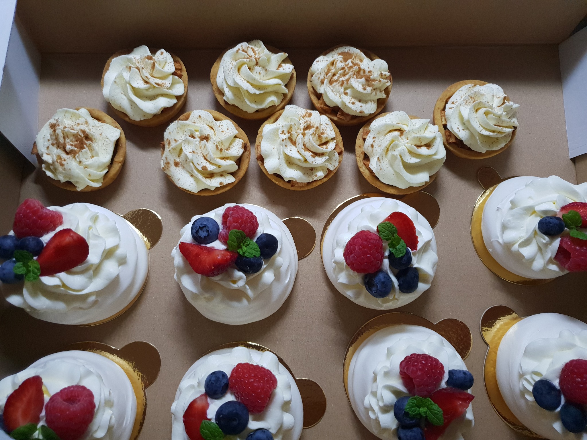 Eleganckie pudełko z tartaletkami z kremem i cynamonem oraz bezami z bitą śmietaną i owocami: truskawkami, malinami i borówkami.