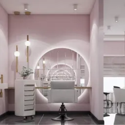 Eleganckie wnętrze salonu kosmetycznego w Warszawie, utrzymane w pastelowych różach, z okrągłym podświetlanym lustrem, designerskim oświetleniem i minimalistycznym stanowiskiem do zabiegów.