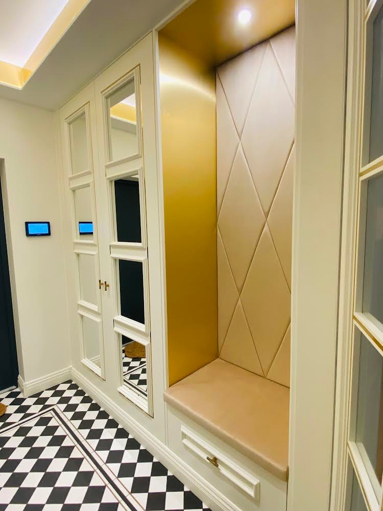 Wnęka z siedziskiem obita beżową tapicerką w romby, złote tło wnęki i biała zabudowa z lustrami na ścianie, podłoga w czarno-białą szachownicę.