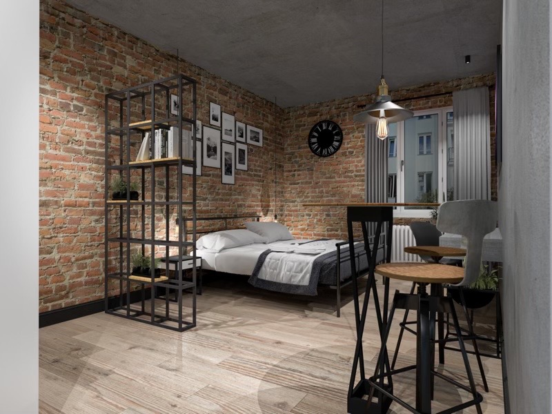 Loftowa sypialnia z ceglaną ścianą, metalowym regałem i łóżkiem, drewnianą podłogą oraz wiszącą lampą z żarówką Edisona.