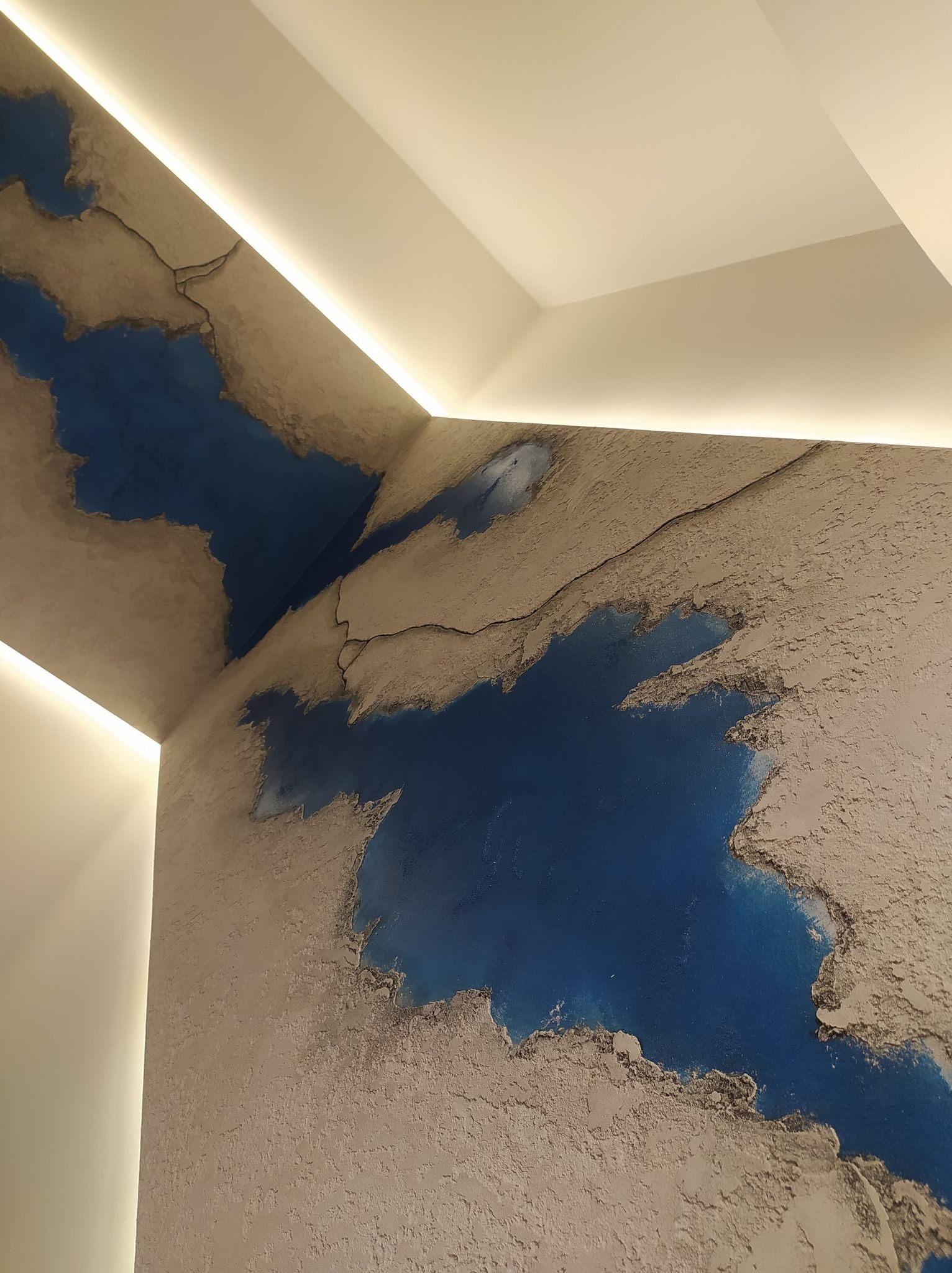 Artystyczna ściana z efektem mapy świata w odcieniach beżu i błękitu, podświetlona ledowym oświetleniem sufitowym.