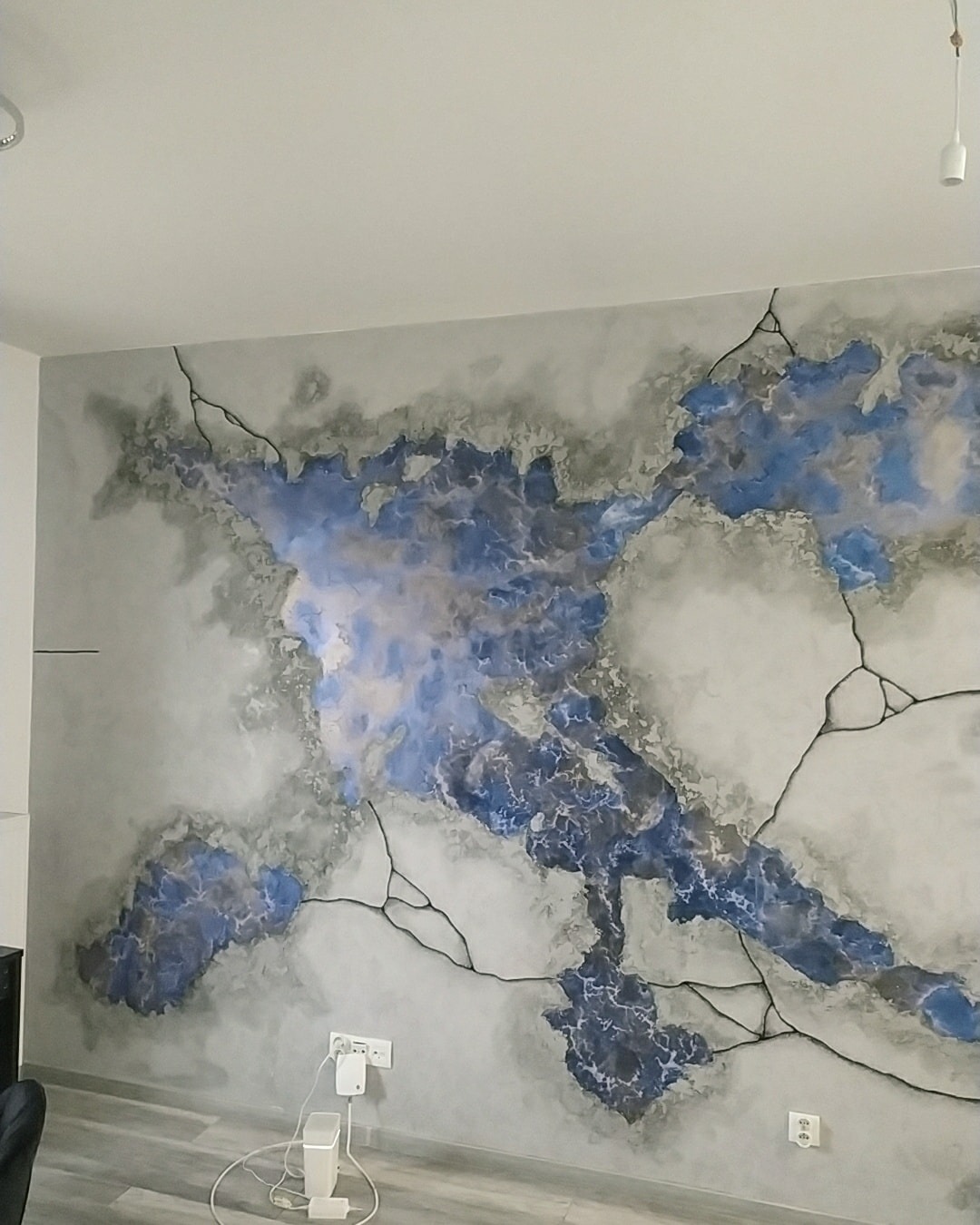 Ściana z dekoracyjnym malowaniem imitującym mapę świata w odcieniach szarości i błękitu z czarnymi liniami spękań.