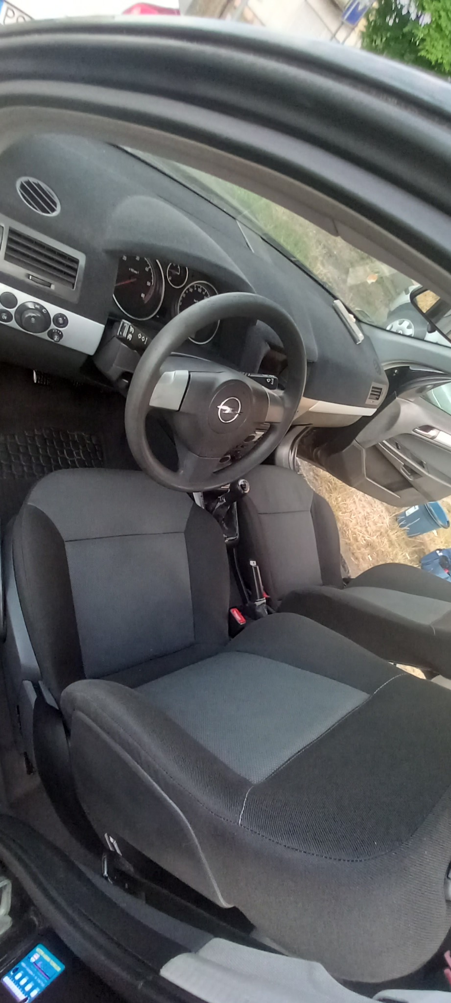 Wnętrze samochodu Opel Astra z widocznymi szarymi fotelami tapicerowanymi, deską rozdzielczą i kierownicą z logo Opel. Widok z perspektywy kierowcy.