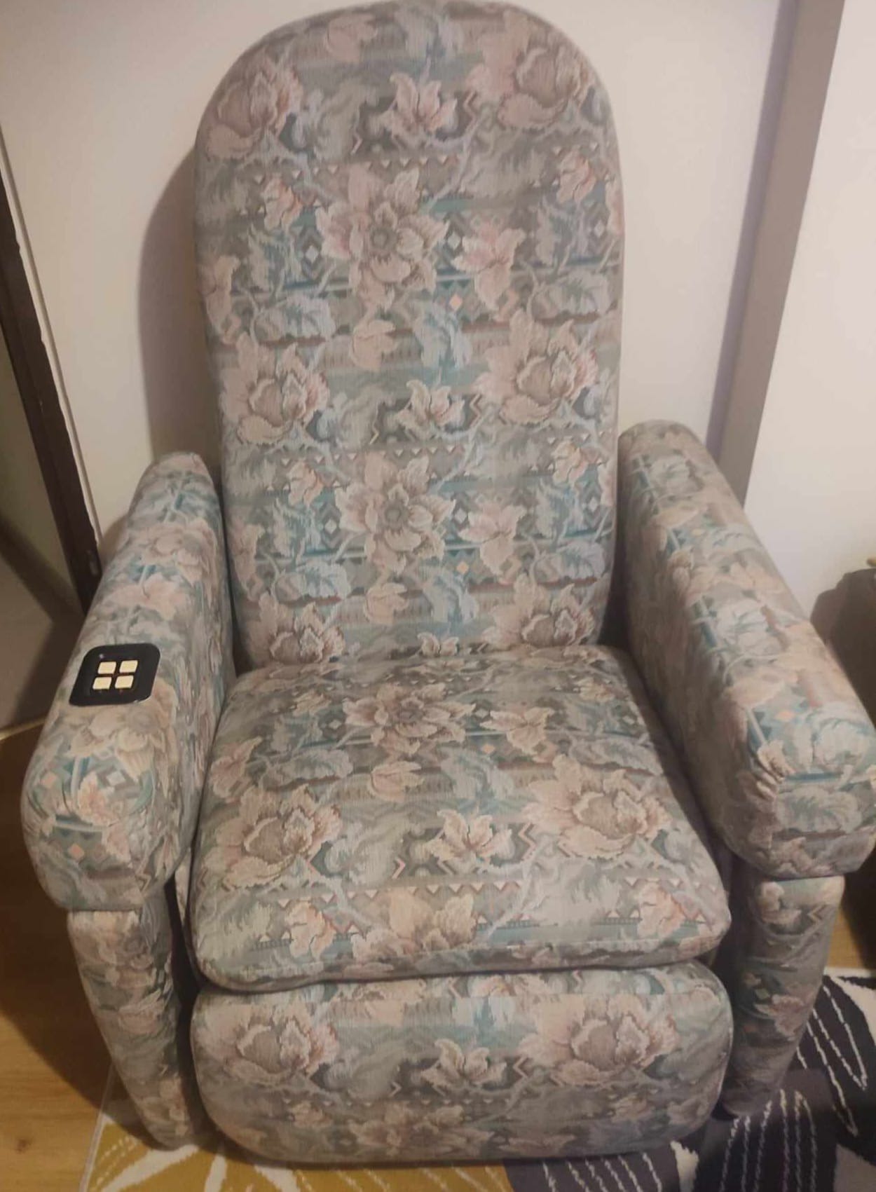 Welurowy fotel z kwiatowym wzorem, z elektryczną regulacją na podłokietniku, ustawiony w pomieszczeniu na dywanie. Widok z przodu.