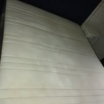 Jasna, czysta tapicerka kanapy z delikatnymi przeszyciami, widoczna pod kątem, po profesjonalnym czyszczeniu, z ciemnym tłem.