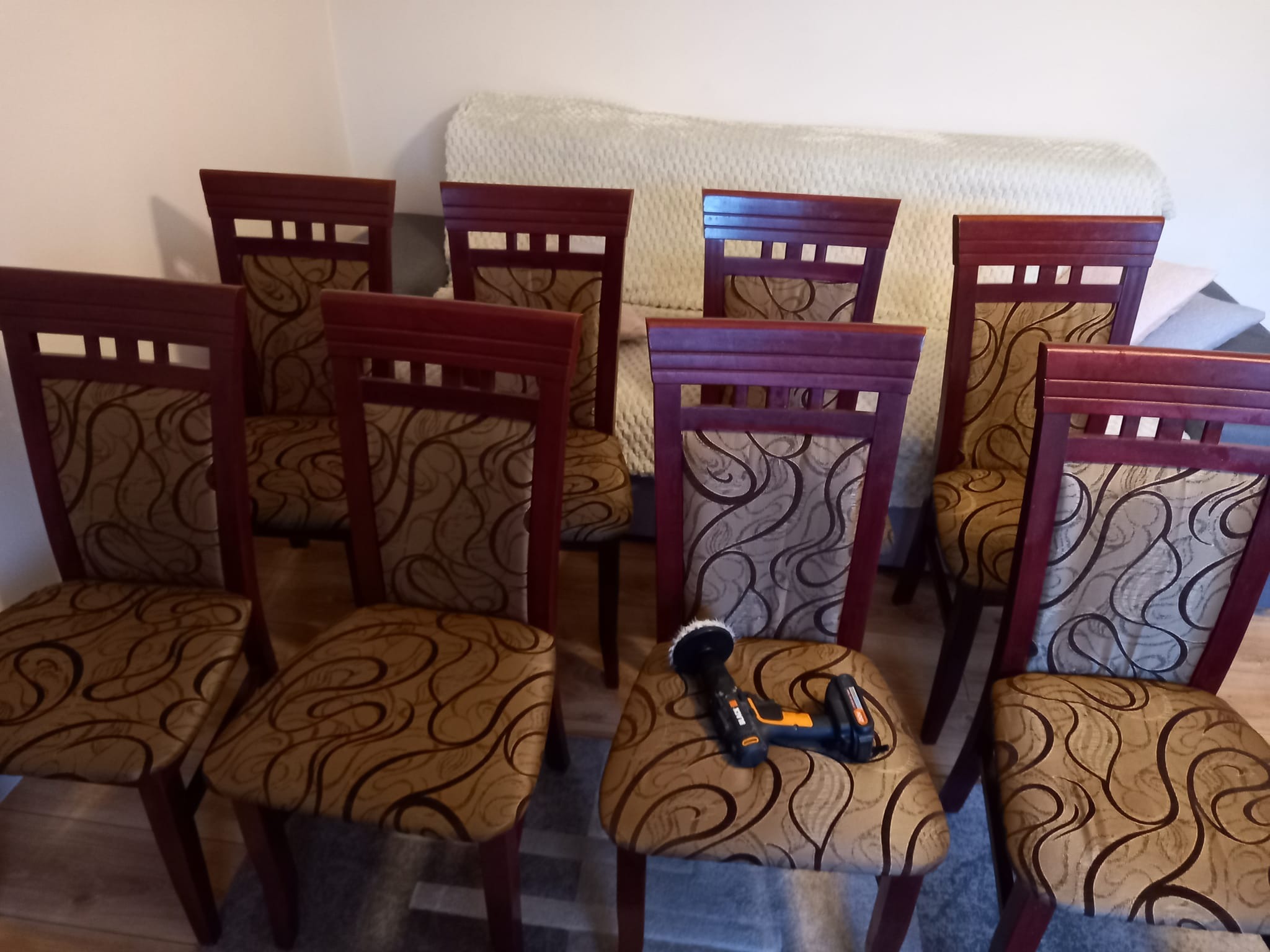 Kilkanaście krzeseł z brązową tapicerką i drewnianymi ramami. Na jednym z siedzisk leży czarno-pomarańczowa polerka do tapicerki.