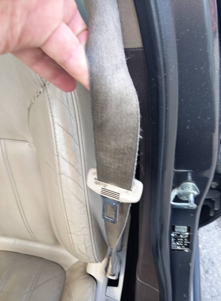 Brudny pas bezpieczeństwa i skórzane siedzenie w aucie przed czyszczeniem. Widoczne ślady użytkowania i zabrudzenia na tapicerce oraz pasie.