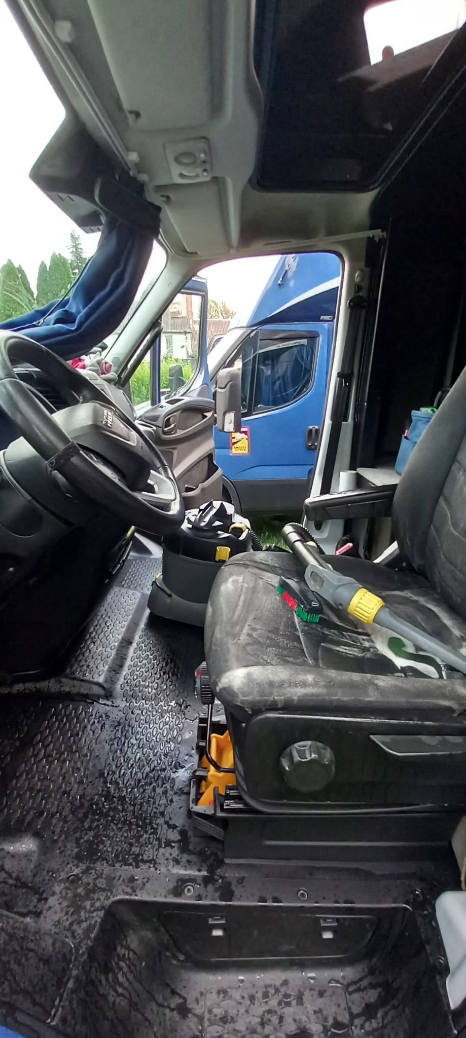 Wnętrze busa po czyszczeniu: mokra podłoga z gumową fakturą, fotel kierowcy z śladami detergentu, widoczny odkurzacz i narzędzia do czyszczenia tapicerki.