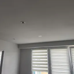 Pomalowany na szaro sufit z zamontowanymi punktowymi lampami LED, widoczne okna z żaluzjami poziomymi.