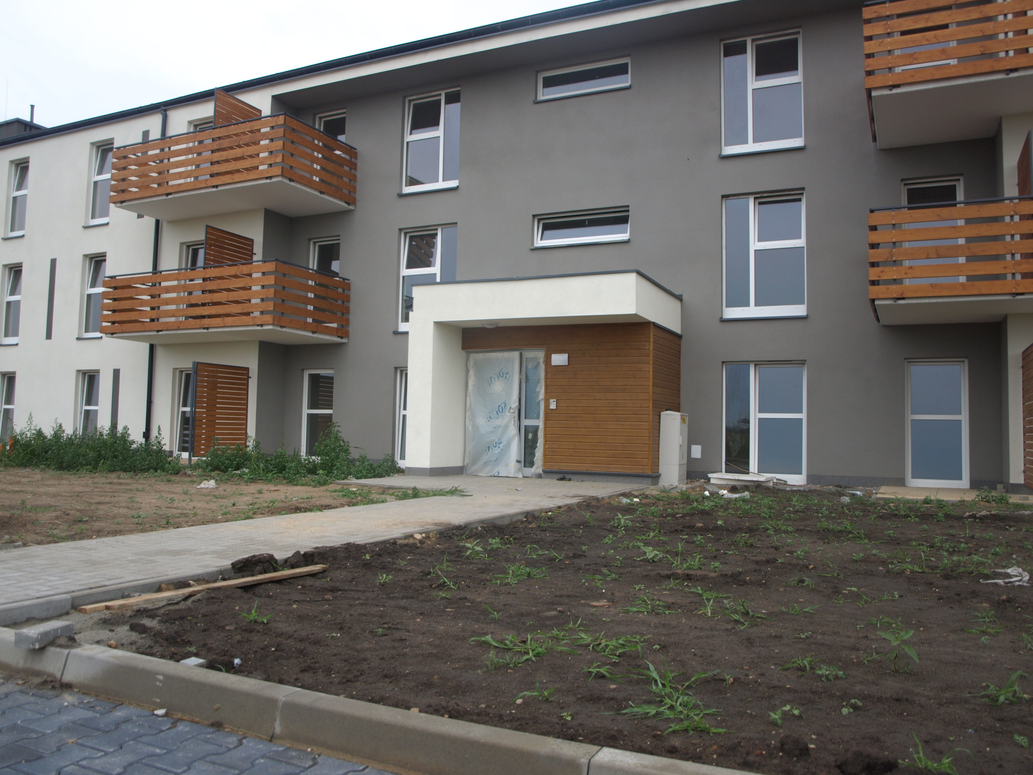 Nowy budynek mieszkalny z przygotowanym terenem pod przyszły ogród, widoczne świeżo ułożone obrzeża i częściowo zagospodarowana ziemia z młodymi roślinami.