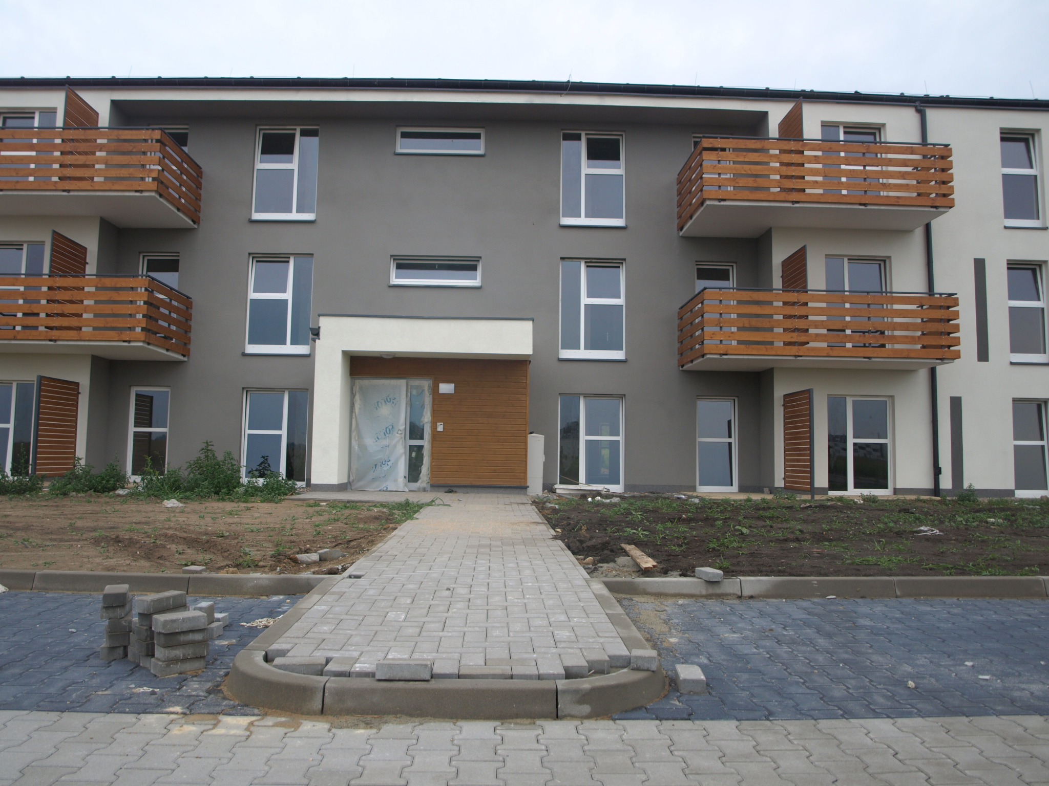 Nowe osiedle mieszkaniowe z częściowo ułożoną kostką brukową na chodniku i parkingu, z widocznymi stertami kostki do dalszego układania.